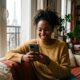 Jeune femme antillaise souriante regardant sa bio site de rencontre sur son smartphone.